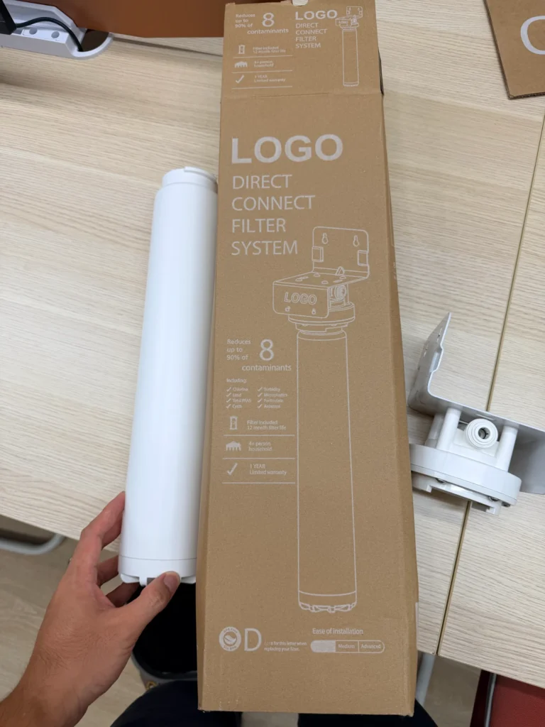Direct connect filter system packaging box and cylindrical filter unit on a light wood table. Male hand holds the filter component.
