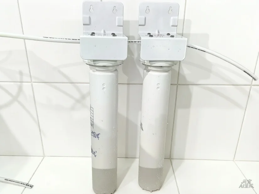 A dual water filter system mounted on a white tiled wall, featuring two cylindrical filters with attached cartridges and piping.