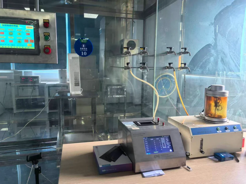 A laboratory setup featuring testing equipment, control panels, glass chambers, and connected tubing in a controlled environment.